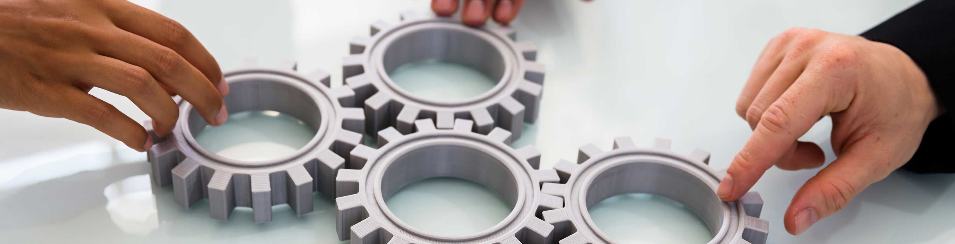 Drei Hände schieben Zahnräder ineinander