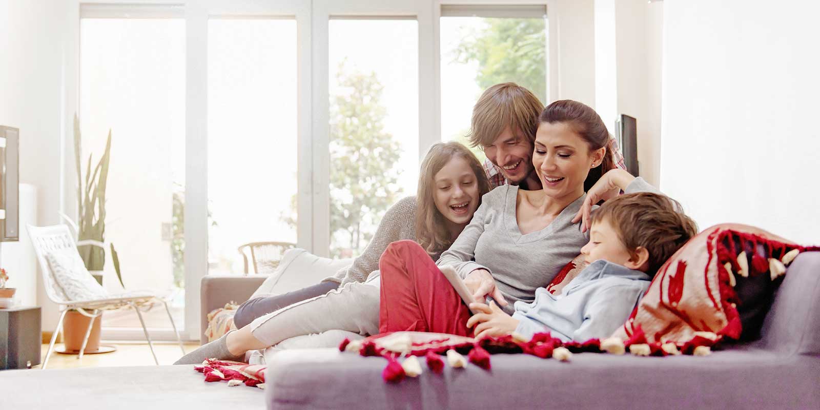 Eltern sitzen mit ihren beiden Kindern auf dem Sofa und schauen auf ein Tablet.